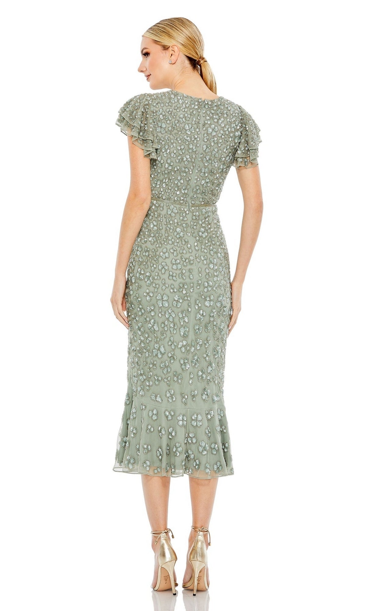 A woman faces away, wearing the Mac Duggal Short Wedding Guest Dress 10771 in light green with flutter sleeves and a ruffled hem, paired with metallic high-heeled sandals.